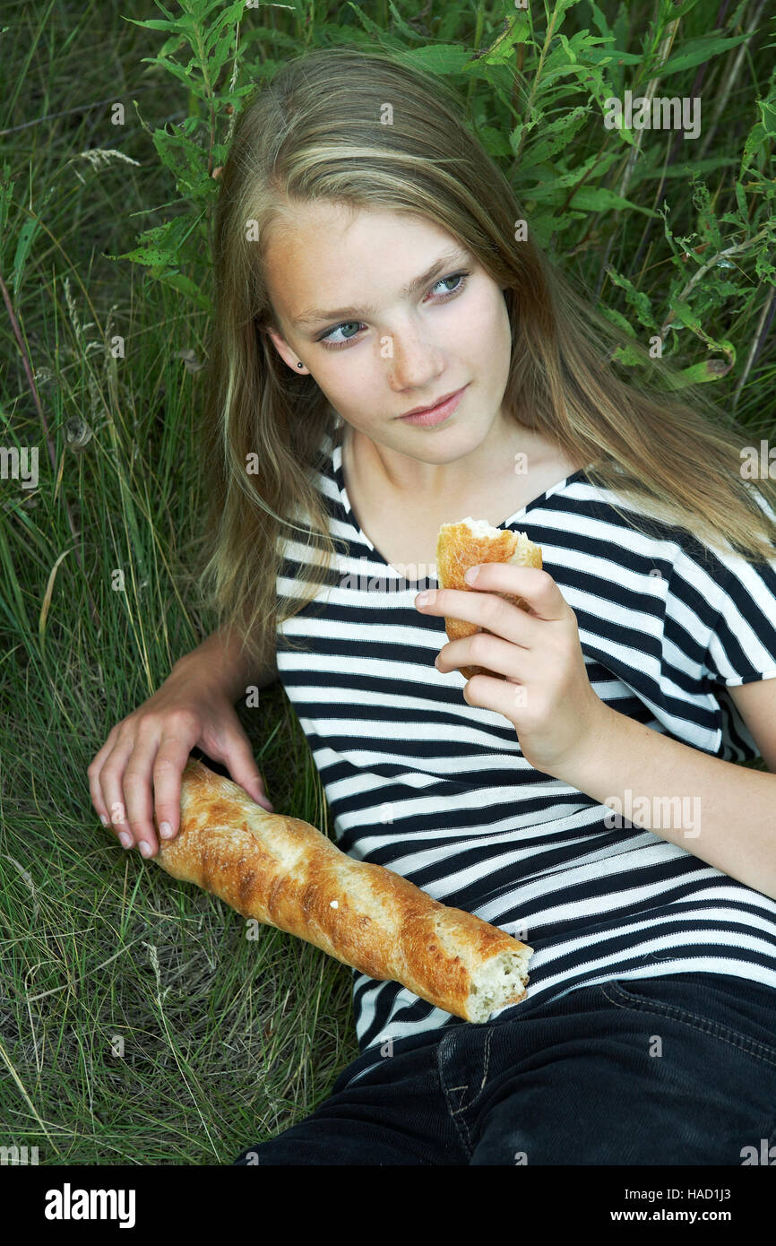 Teen mangiando pane francese in un prato. Foto Stock