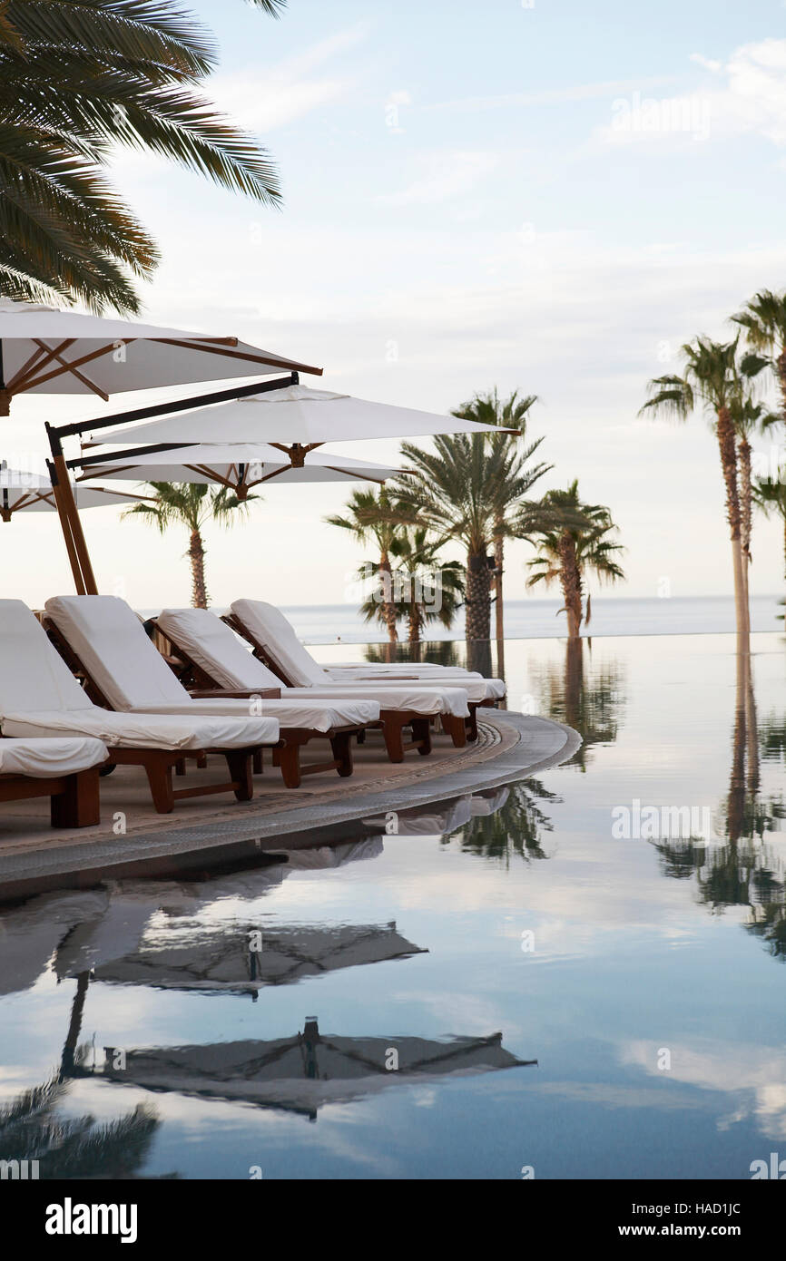 Chaise longue, palme e ombrelloni vicino alla piscina infinity a Cabo San Lucas, Baja, Messico Foto Stock