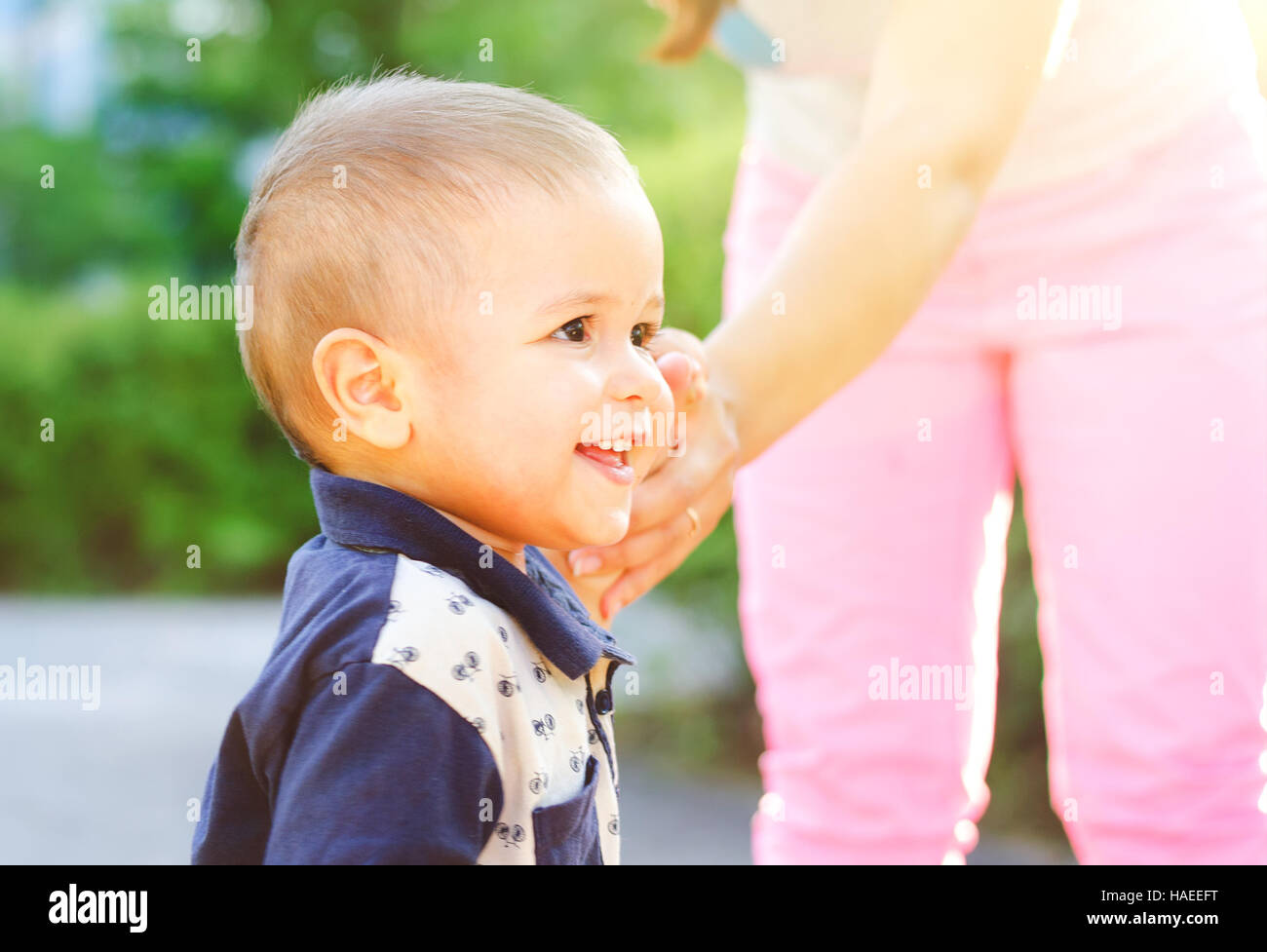 Ritratto di un piccolo ragazzo sorridente camminando con sua madre la mano all'esterno. Passeggiata nella natura con la luce del sole. Foto Stock