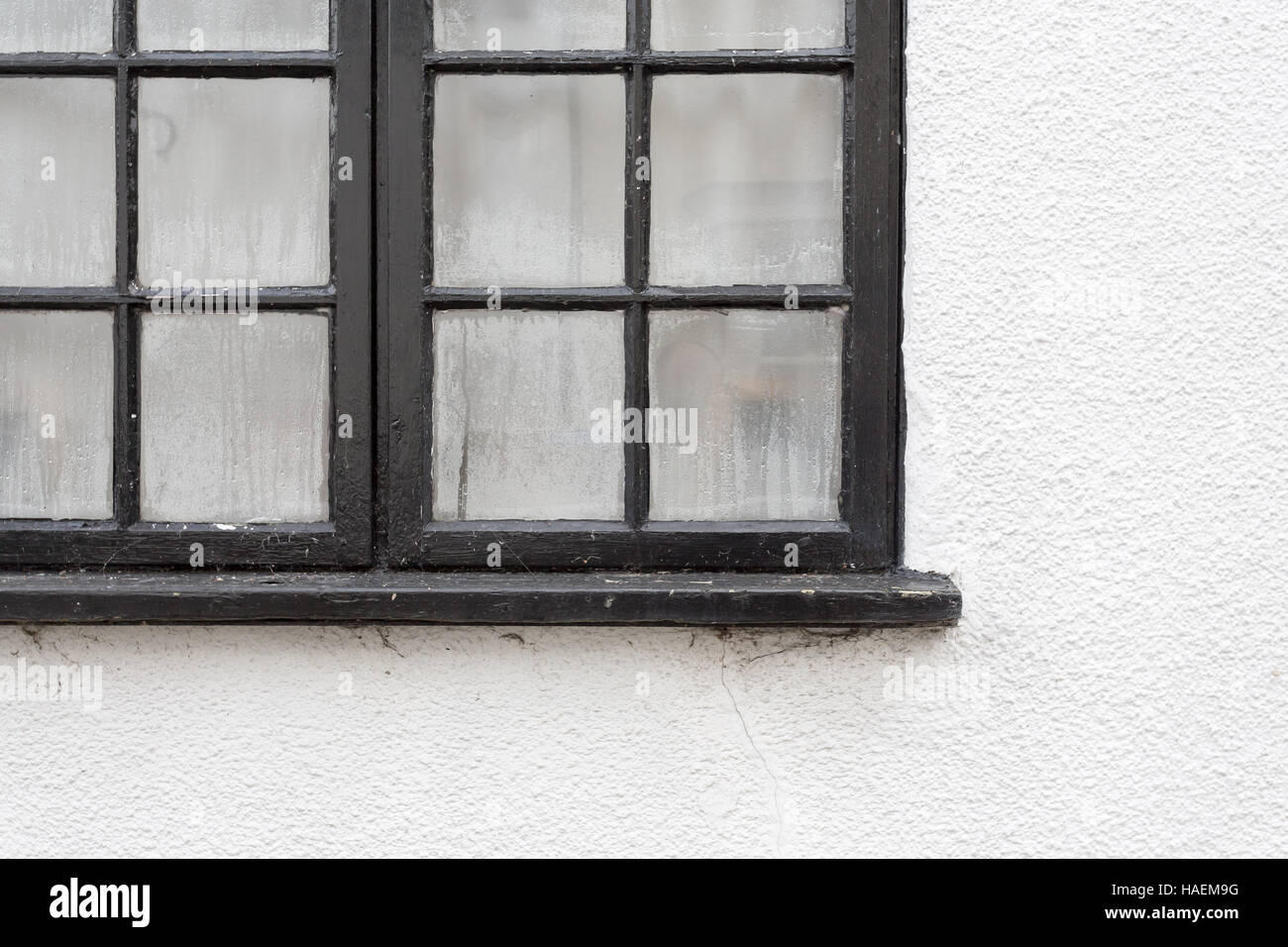 Il nero sul telaio di una finestra con gocce di condensa sul dipinto di bianco parete cottage, spazio di copia Foto Stock