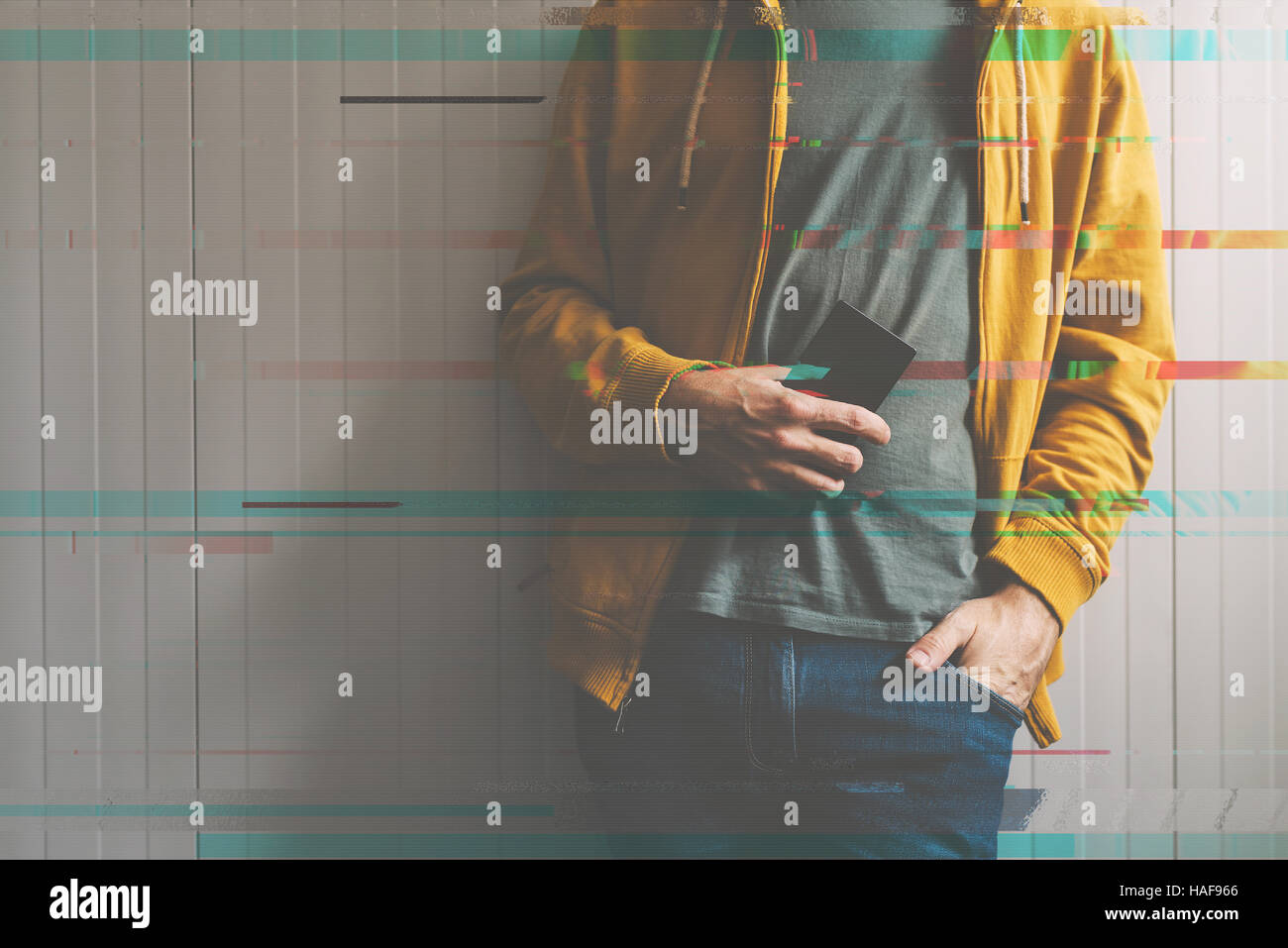 Casual giovane uomo in posa con il cellulare in mano, la tecnologia e il concetto di stile di vita, dai toni rétro immagine digitale con effetto di glitch Foto Stock
