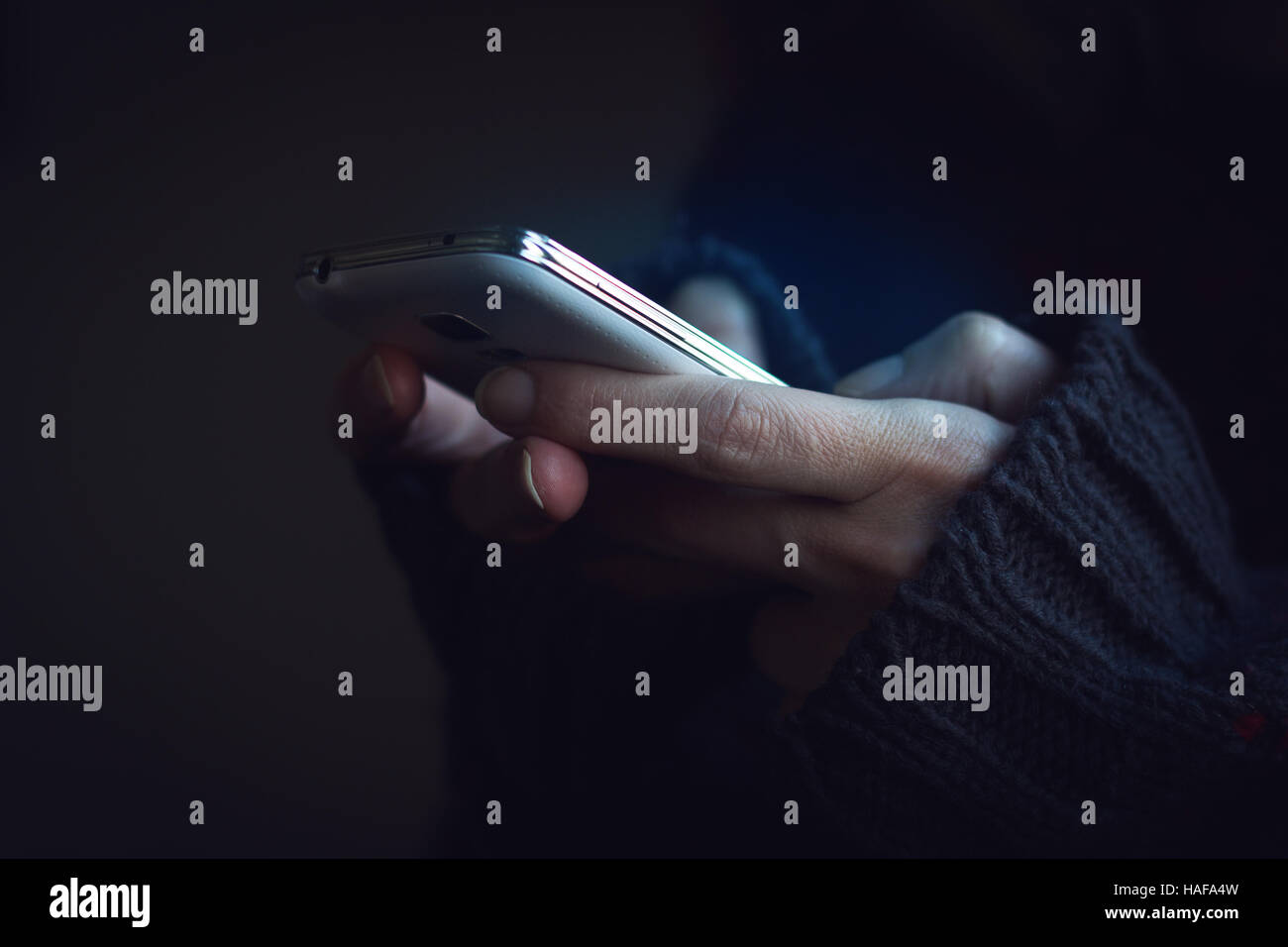 Vista frontale ravvicinata di una donna le mani nel buio maglione mani tenendo un telefono e digitando Foto Stock