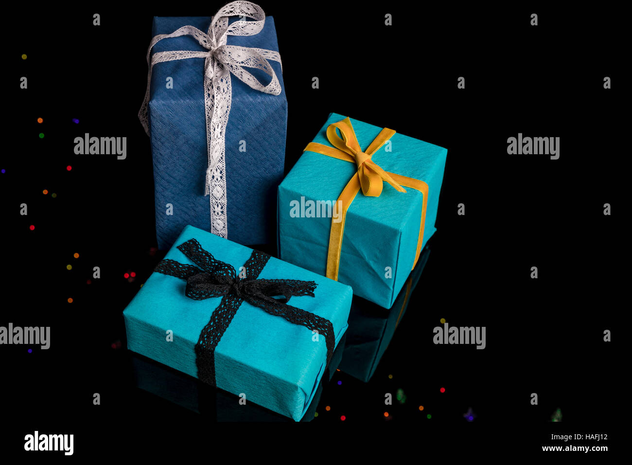Tre presenta di diverse dimensioni avvolti in blu e turchese carta testurizzata legato con pizzi e nastri di velluto su nero Foto Stock