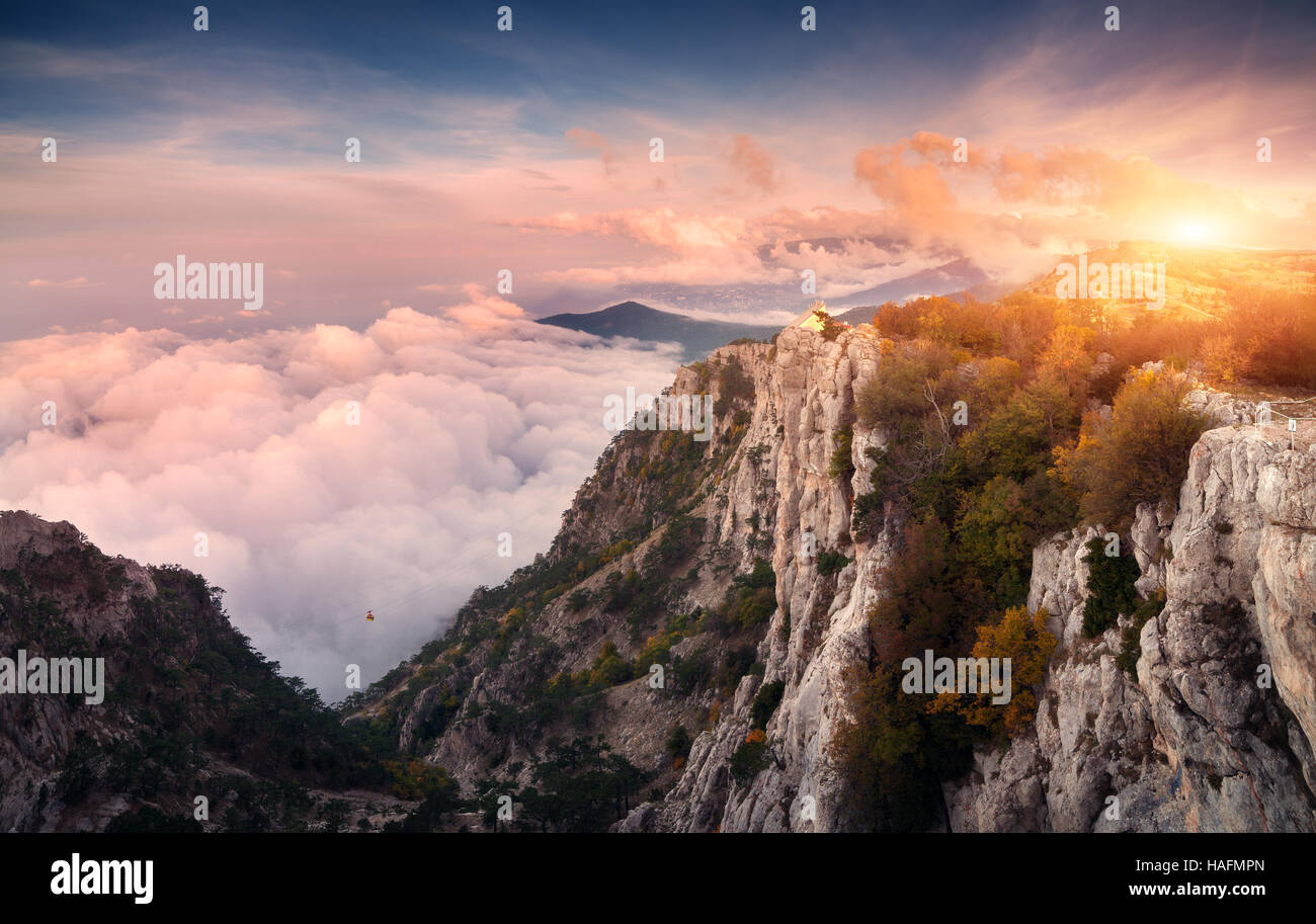 Panoramica del paesaggio di montagna al tramonto. Incredibile vista dal picco di montagna sulle alte rocce, cielo, nuvole e alberi di sera Foto Stock