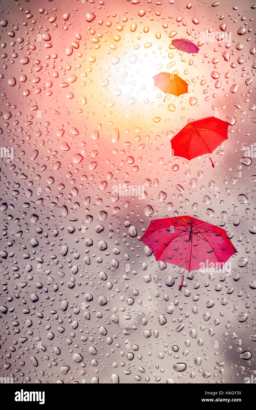 Flusso di ombrelloni nel cielo con la caduta di pioggia e di luce solare Foto Stock