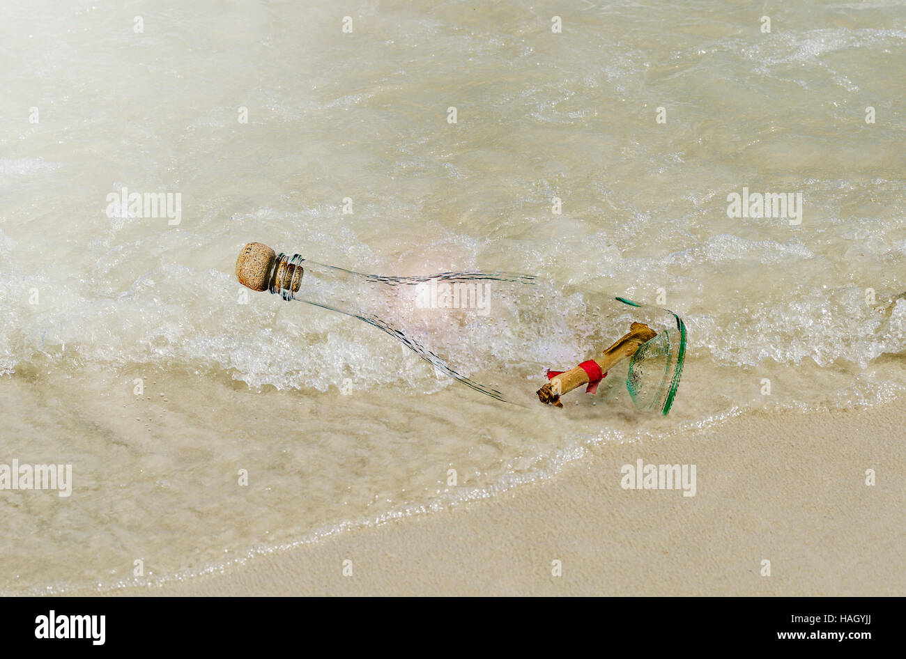 Carta in rotolo con corda rossa all'interno di una bottiglia di vetro sulla spiaggia sotto la luce del sole. Foto Stock