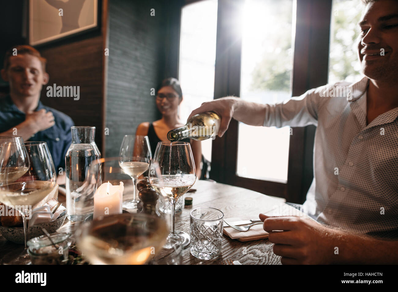Gruppo di amici gustando un pasto con il vino al ristorante. Felice giovane versando il vino in bicchieri. Foto Stock