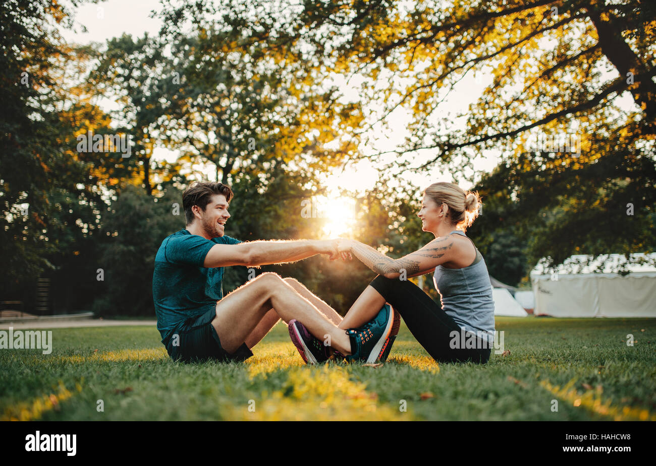 Sano giovane uomo e donna seduta insieme tenendo le mani e di stiro. Coppia giovane esercitare insieme al parco. Foto Stock