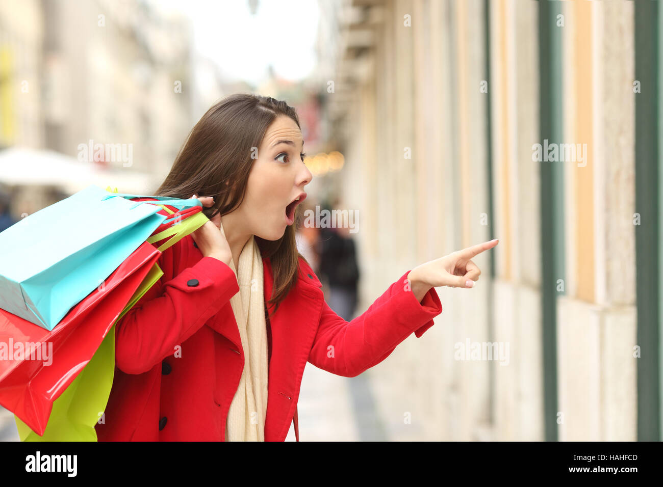 Stupiti shopper bocca di apertura azienda borse per lo shopping a guardare le offerte speciali nei negozi e puntamento in strada in inverno Foto Stock