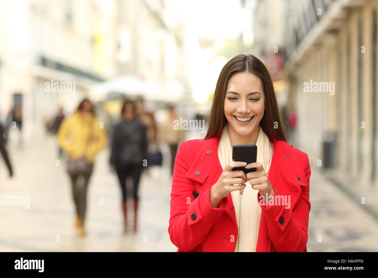 Vista frontale di una moda donna che indossa cappotto rosso utilizzando uno smartphone in inverno e camminare verso la telecamera Foto Stock