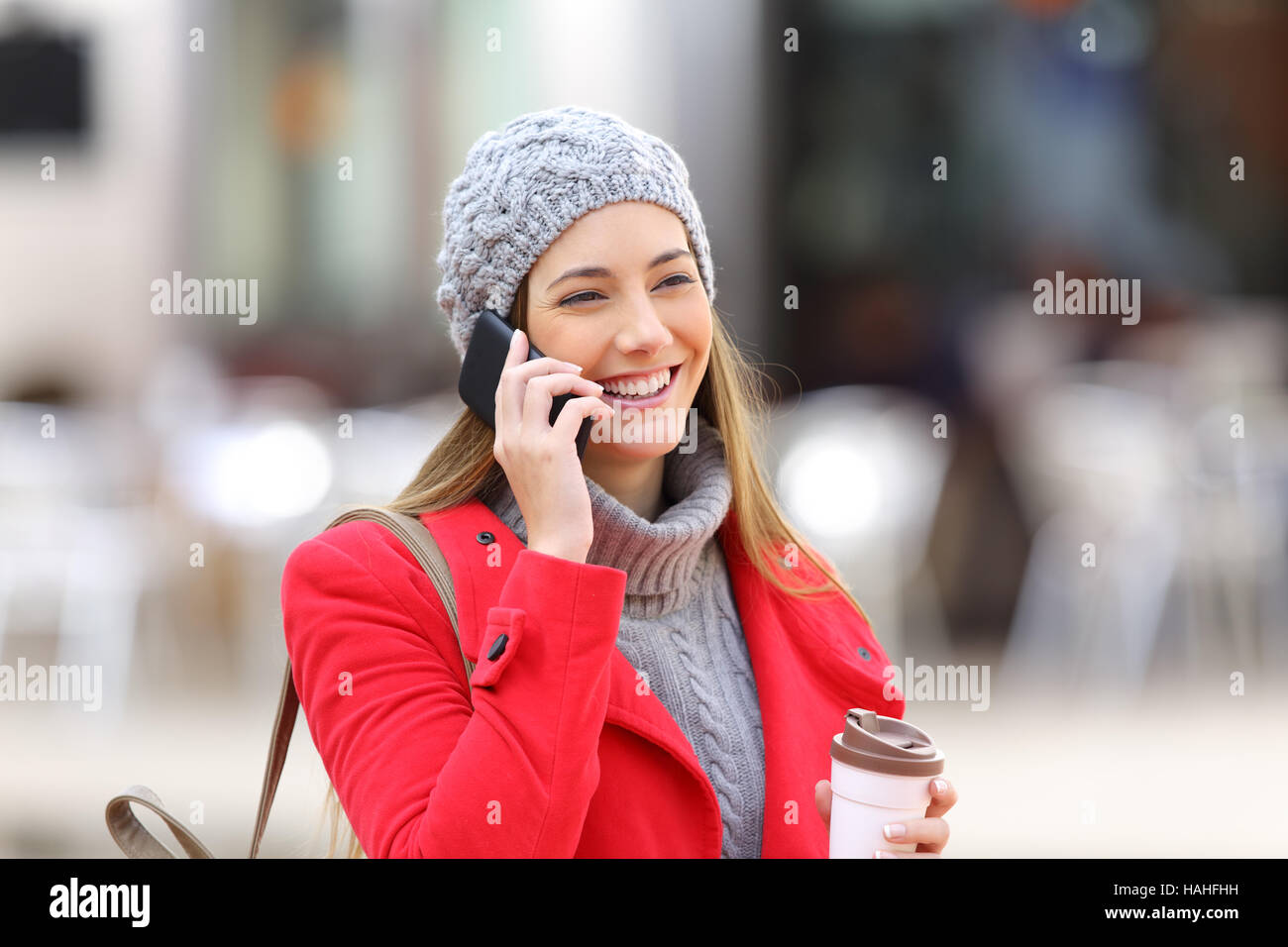 Donna felice chiamando al telefono cellulare e tenendo un take away caffè in strada in inverno Foto Stock