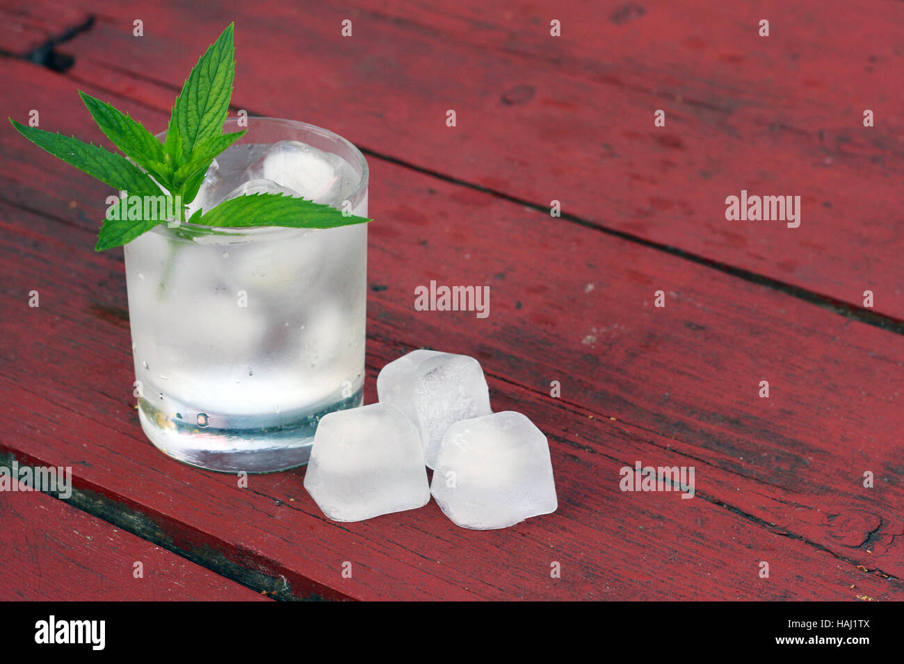 Bicchiere di acqua con cubetti di ghiaccio e menta sul vecchio tavolo in legno Foto Stock