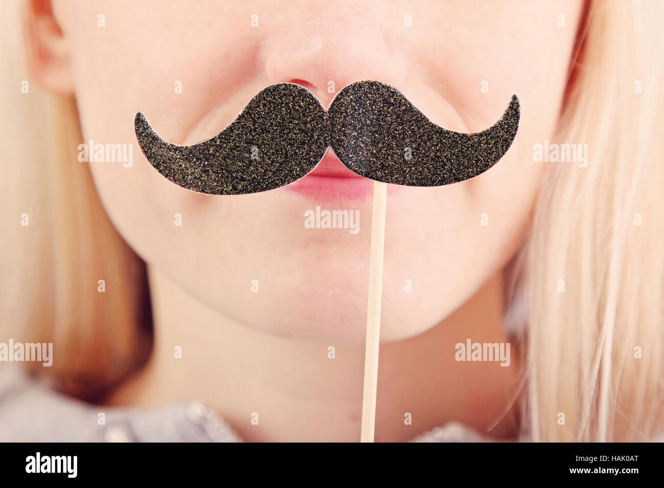Donna che mantiene i baffi su un bastone davanti al suo volto Foto Stock