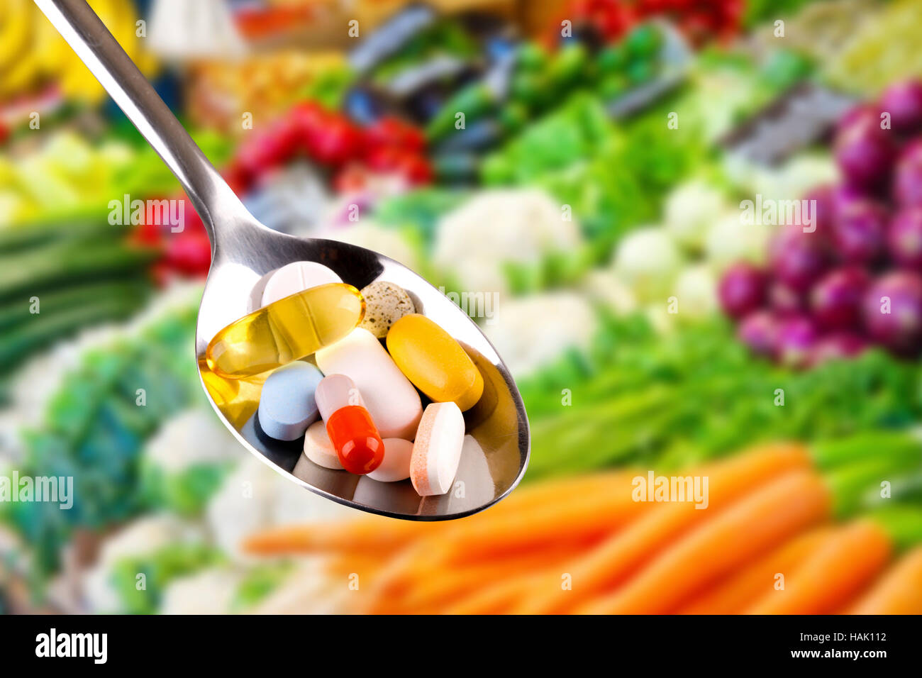 Cucchiaio con le pillole, integratori dietetici su sfondo di verdure Foto Stock