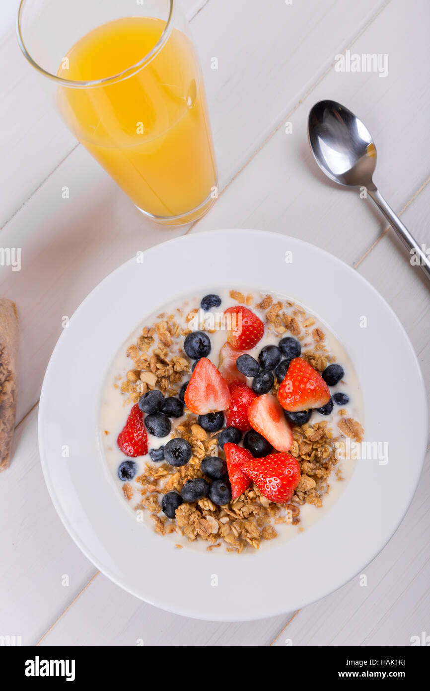 Ciotola con cereali muesli e succhi di arancia sul tavolo bianco Foto Stock