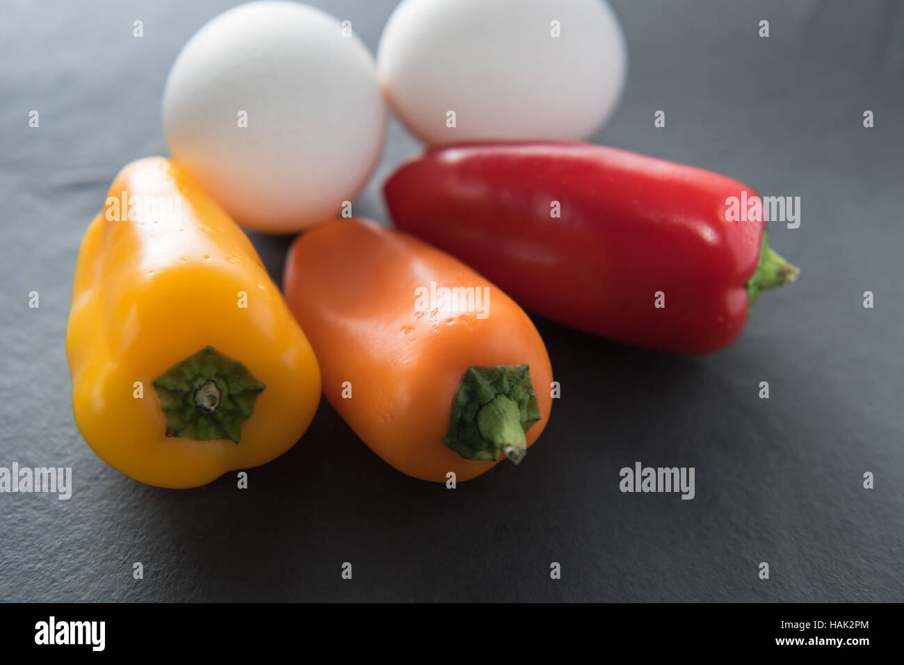 Low Carb - due uova di colore bianco con tre mini colorati paprikas al buio su un sfondo di ardesia - vivida luce. Foto Stock