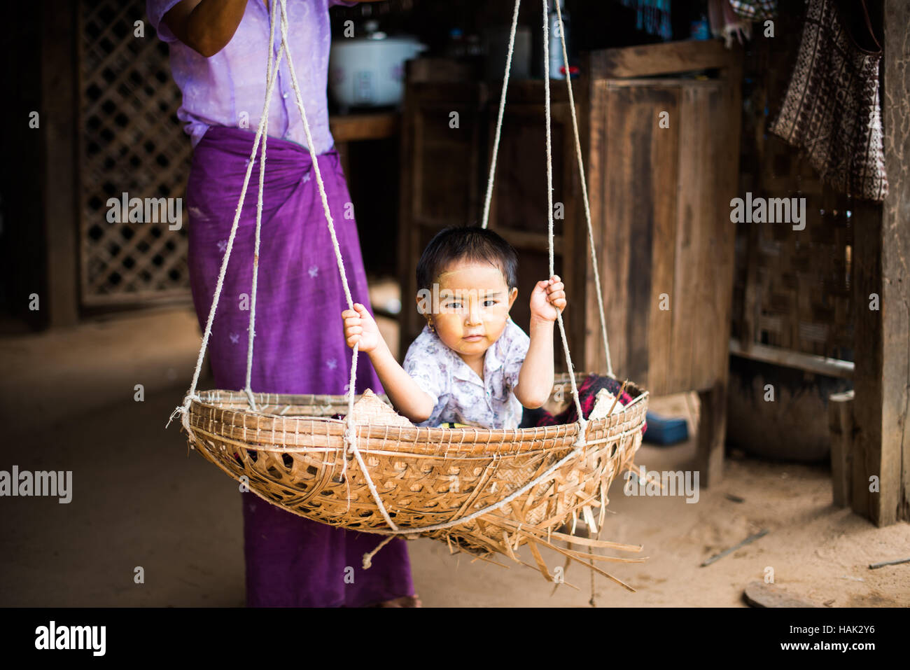 MINNANTHU, Myanmar — Un bambino piccolo oscilla in un cesto intrecciato nel villaggio di Minnanthu a Bagan, Myanmar. Adagiato tra le rovine archeologiche della piana di Bagan, il minuscolo villaggio di Minnanthu conserva lo stile di vita tradizionale. Foto Stock