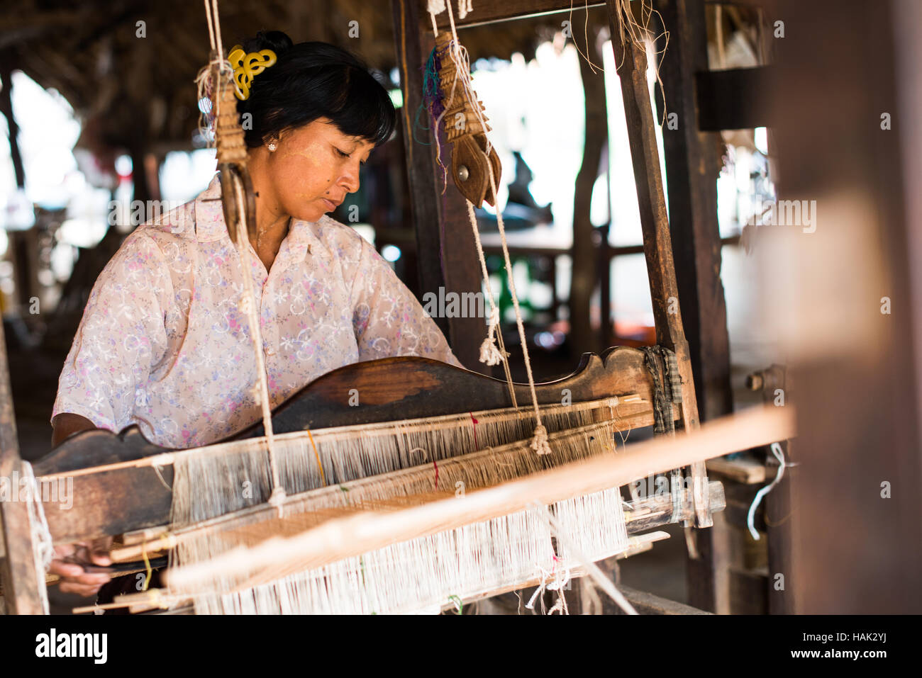 Tessitura tradizionale Loom Minnanthu Village Myanmar // MINNANTHU, Myanmar — Una donna utilizza un telaio tradizionale per tessere tessuti nel villaggio di Minnanthu, situato all'interno della zona archeologica di Bagan nel Myanmar centrale. Il villaggio si trova tra le antiche rovine del tempio della zona archeologica di Bagan, che contiene oltre 2.000 templi buddisti e pagode risalenti all'XI-XIII secolo. Il villaggio di Minnanthu conserva artigianato tradizionale e stili di vita nonostante sia circondato da uno dei siti archeologici più significativi del Myanmar. La pianura di Bagan, situata lungo il fiume Ayeyarwady (anche k Foto Stock