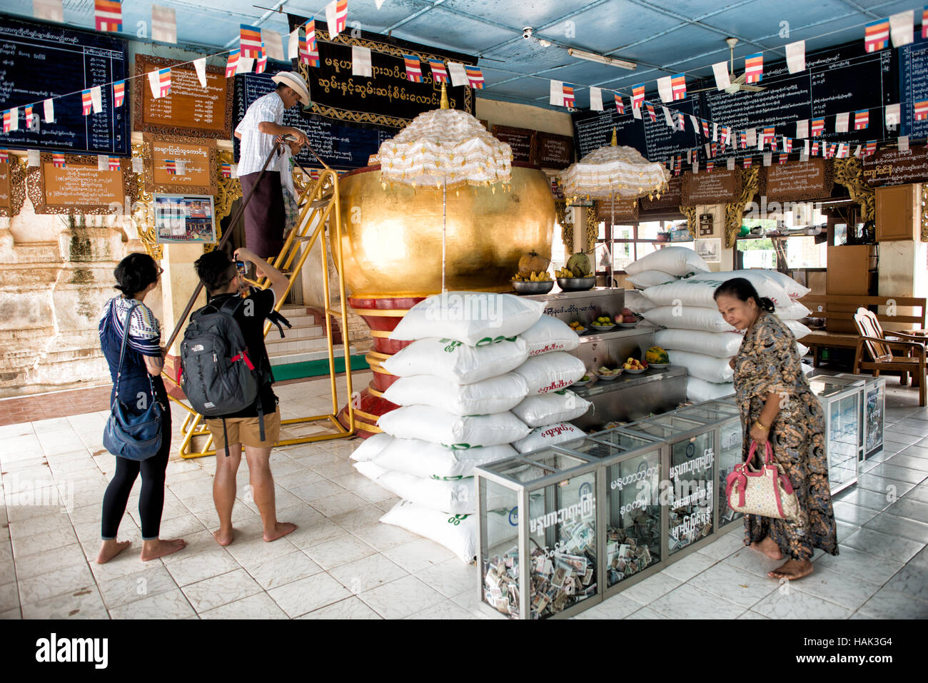 Donazioni del Tempio di Manuha Bagan Myanmar // BAGAN, Myanmar - donazioni di riso e cibo sono offerte al Tempio di Manuha, un monumento buddista costruito nel 1067 d.C. dal prigioniero re Mon Manuha in seguito alla sua sconfitta da re Anawrahta del Regno pagano. Il tempio ospita quattro monumentali immagini di Buddha, tre sedute e una reclinata, deliberatamente posizionate in camere strette che simboleggiano la sofferenza psicologica del re imprigionato. Costruito utilizzando i proventi della vendita del prezioso gioiello maya Manaw di Manuha, il tempio serviva sia a scopi religiosi che pratici, consentendo al re prigioniero di guadagnare m Foto Stock