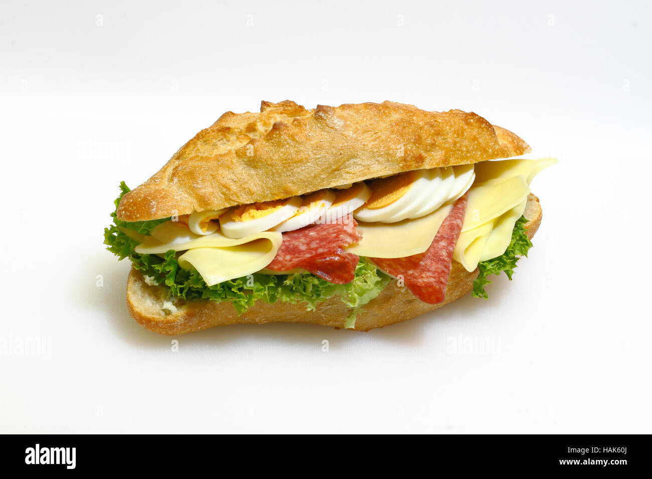 Baguette bun e rabboccato con salame, formaggio, lattuga e uova sode su un bianco tagliere in plastica Foto Stock