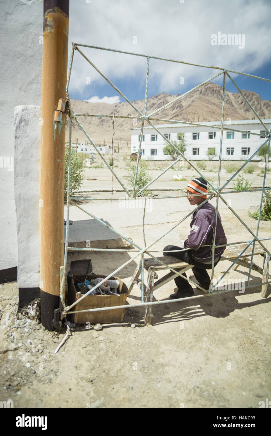 Ragazzo giovane su un banco, dietro un recinto nel cortile della scuola in Murghab,Tagikistan Foto Stock