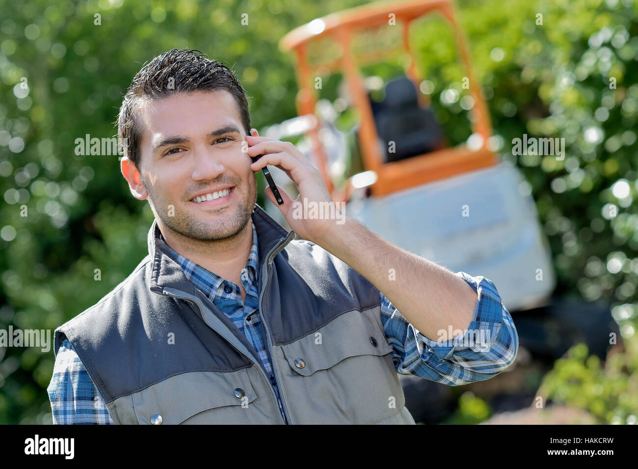 Il giardiniere sul telefono, scavatrice in background Foto Stock