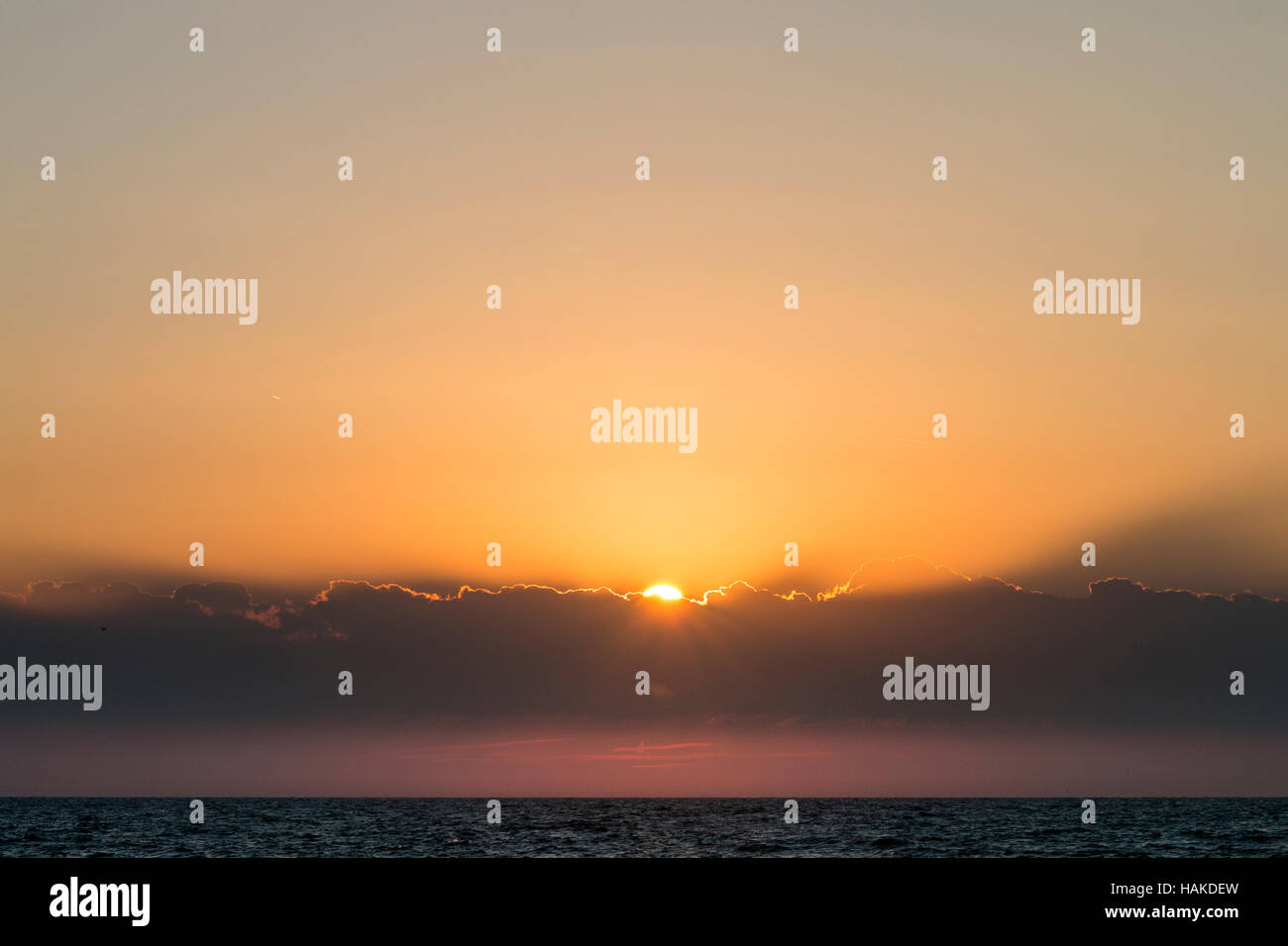 Inghilterra, Broadstairs. All'alba. Il sorgere del sole da dietro il cloud banca nel Canale della Manica. Principalmente giallo arancione del cielo. Foto Stock