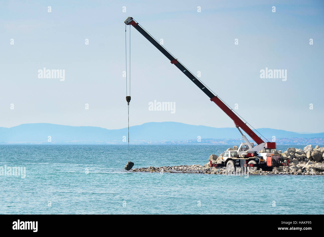 Una gru mobile demolitore onda pietre con la pietra appena a contatto con il mare Foto Stock