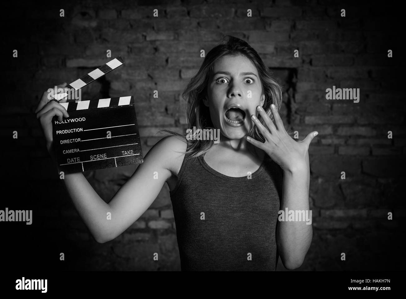 Giovane donna bionda attrice nel seminterrato buio, in bianco e nero scioccato espressione con movie clapper bordo, guardando la fotocamera Foto Stock