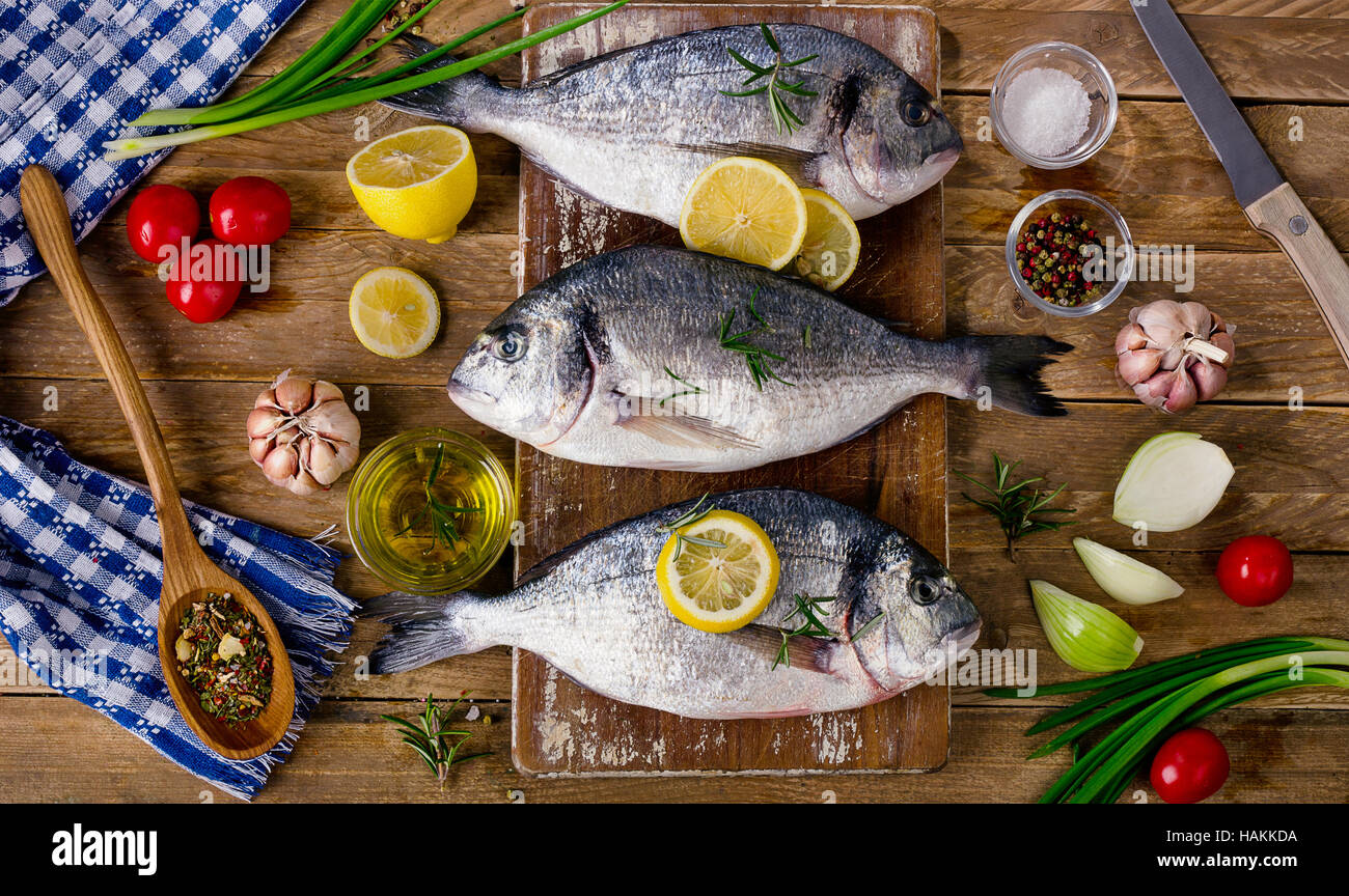 Pesce fresco con erbe aromatiche, spezie e verdure su legno rustico sfondo. Cibo sano concetto. Vista superiore Foto Stock