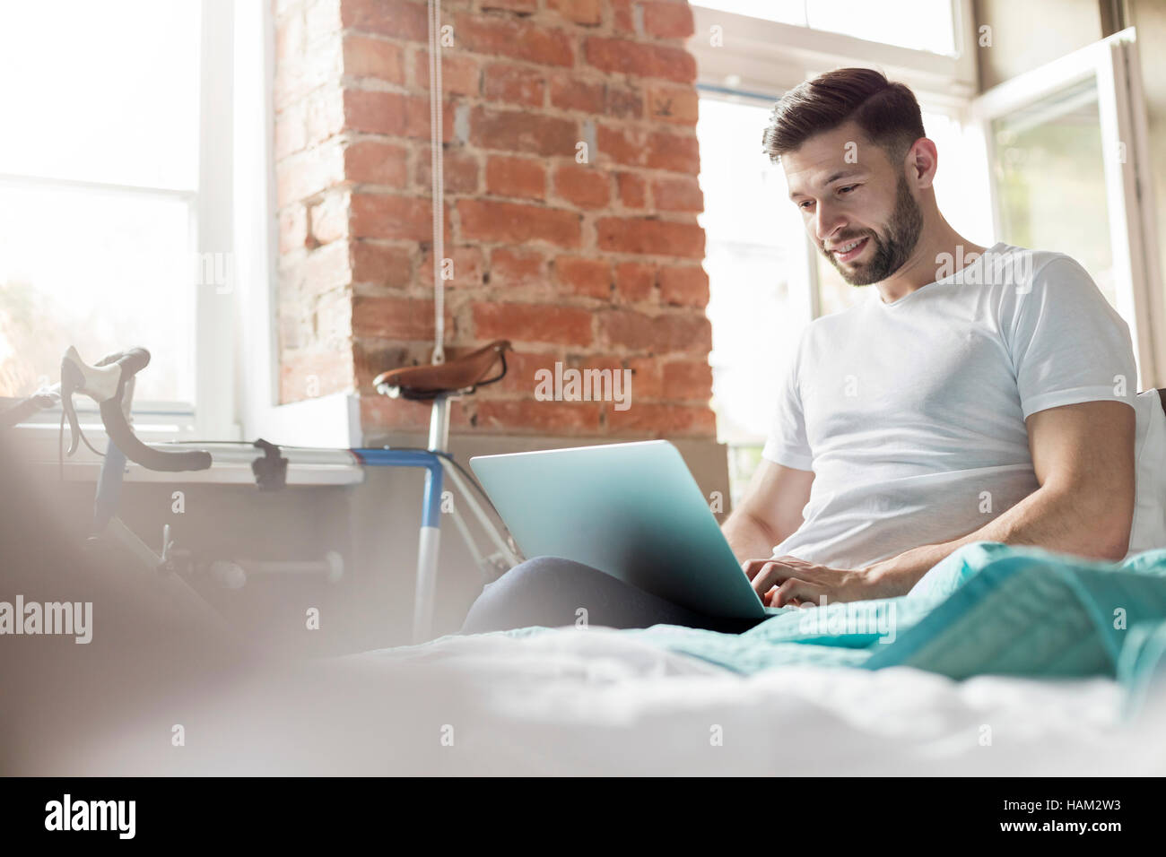 Uomo che utilizza sul computer portatile sul letto in appartamento Foto Stock