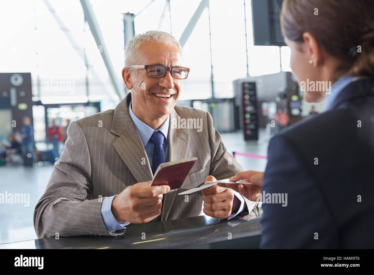 Imprenditore sorridente dando il passaporto per il rappresentante del servizio di assistenza clienti all'aeroporto al banco check-in Foto Stock