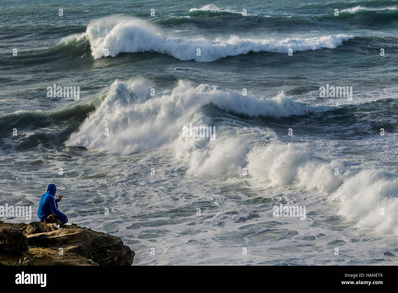 Un uomo orologi di fumare accanto al suo cane all'alba le conseguenze della tempesta sul mare e le grandi onde Foto Stock