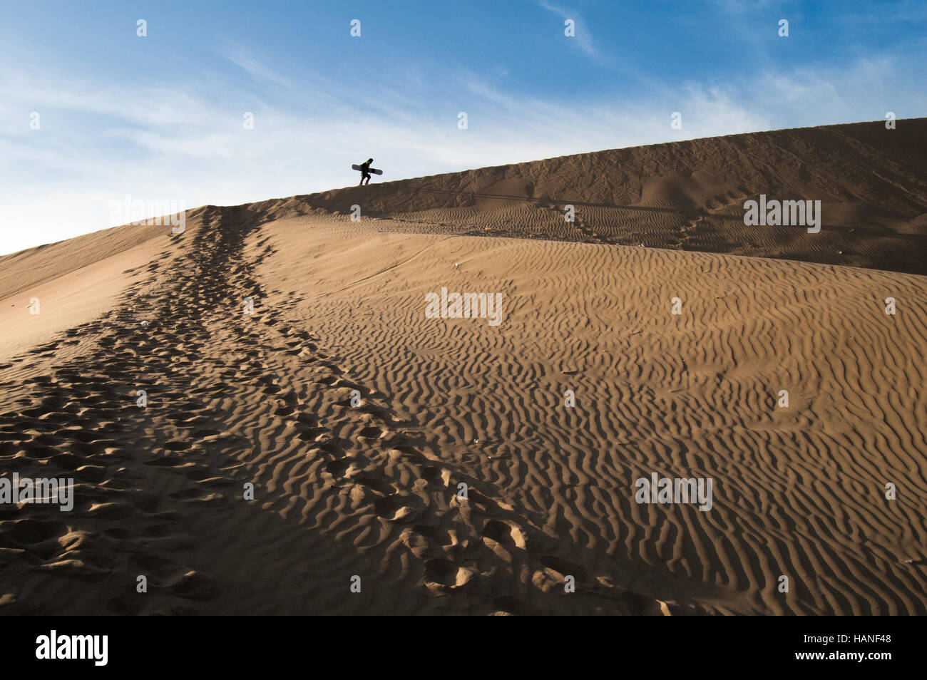Un uomo a piedi su per la collina di Huacachina dune con uno scarpone da snowboard alla pratica sandboard Foto Stock