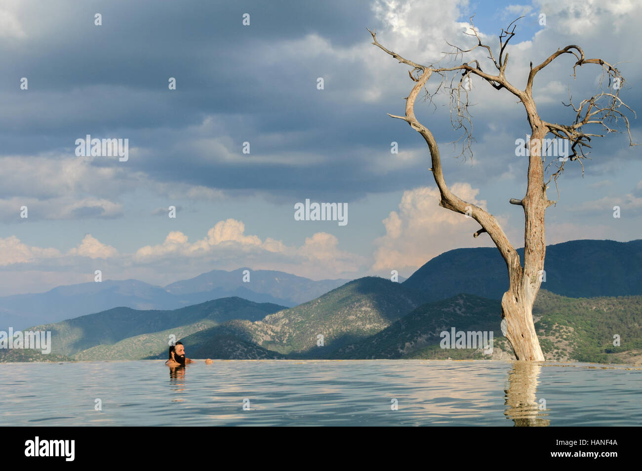 Un uomo caucasico con la barba guarda il paesaggio delle montagne di Oaxaca in una piscina naturale di un orizzonte infinito Foto Stock