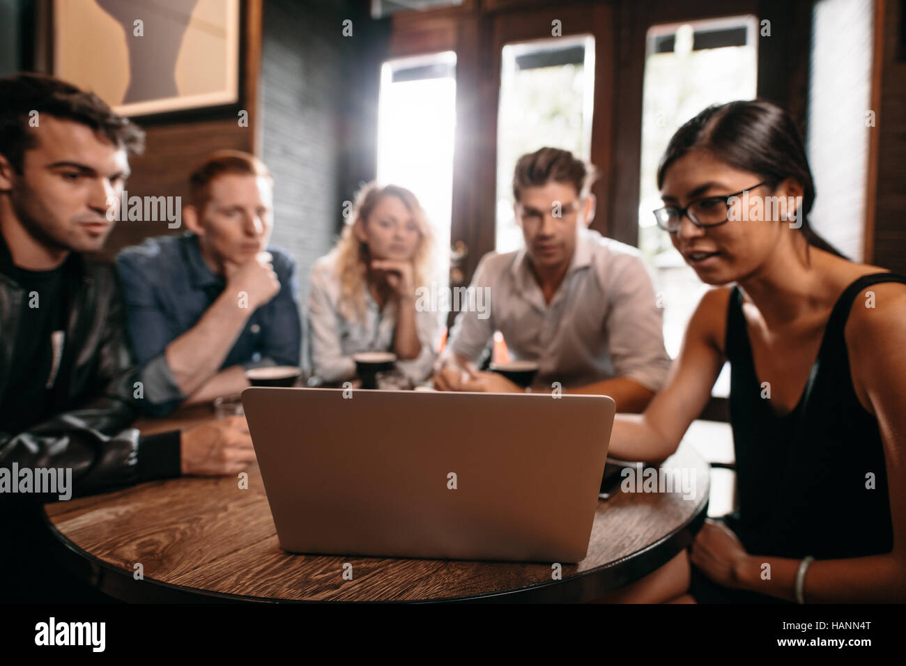 Gruppo di amici seduti attorno al tavolo del bar e guardando il laptop. Giovani uomini e donne presso la caffetteria utilizzando computer portatili. Foto Stock