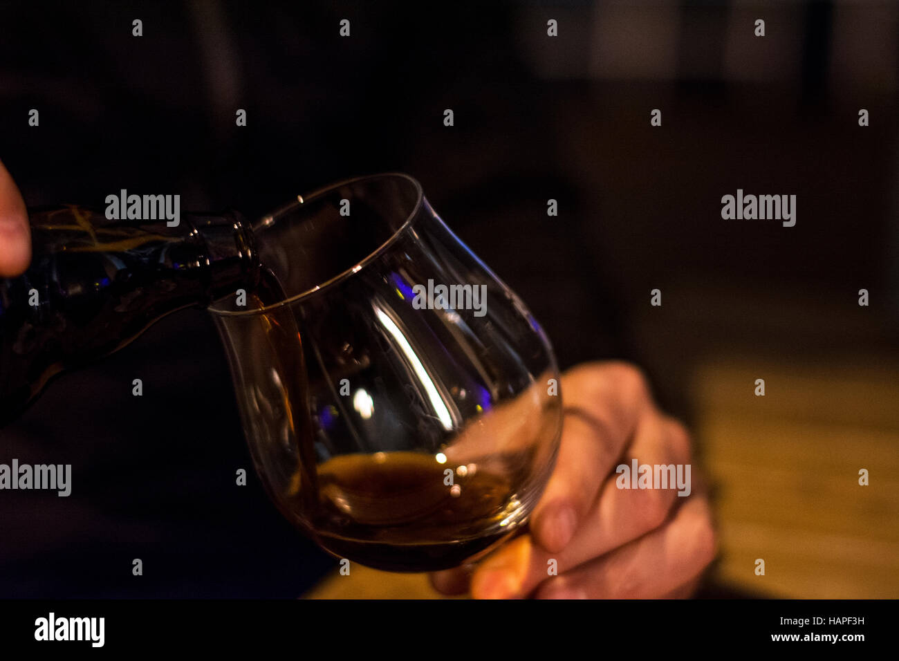 L uomo è nero di versare la birra dalla bottiglia in vetro al caffé Foto Stock