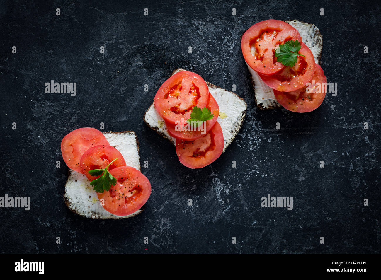 Una sana crostini con ricotta e pomodori freschi sul nero ardesia sfondo. Vista superiore Foto Stock