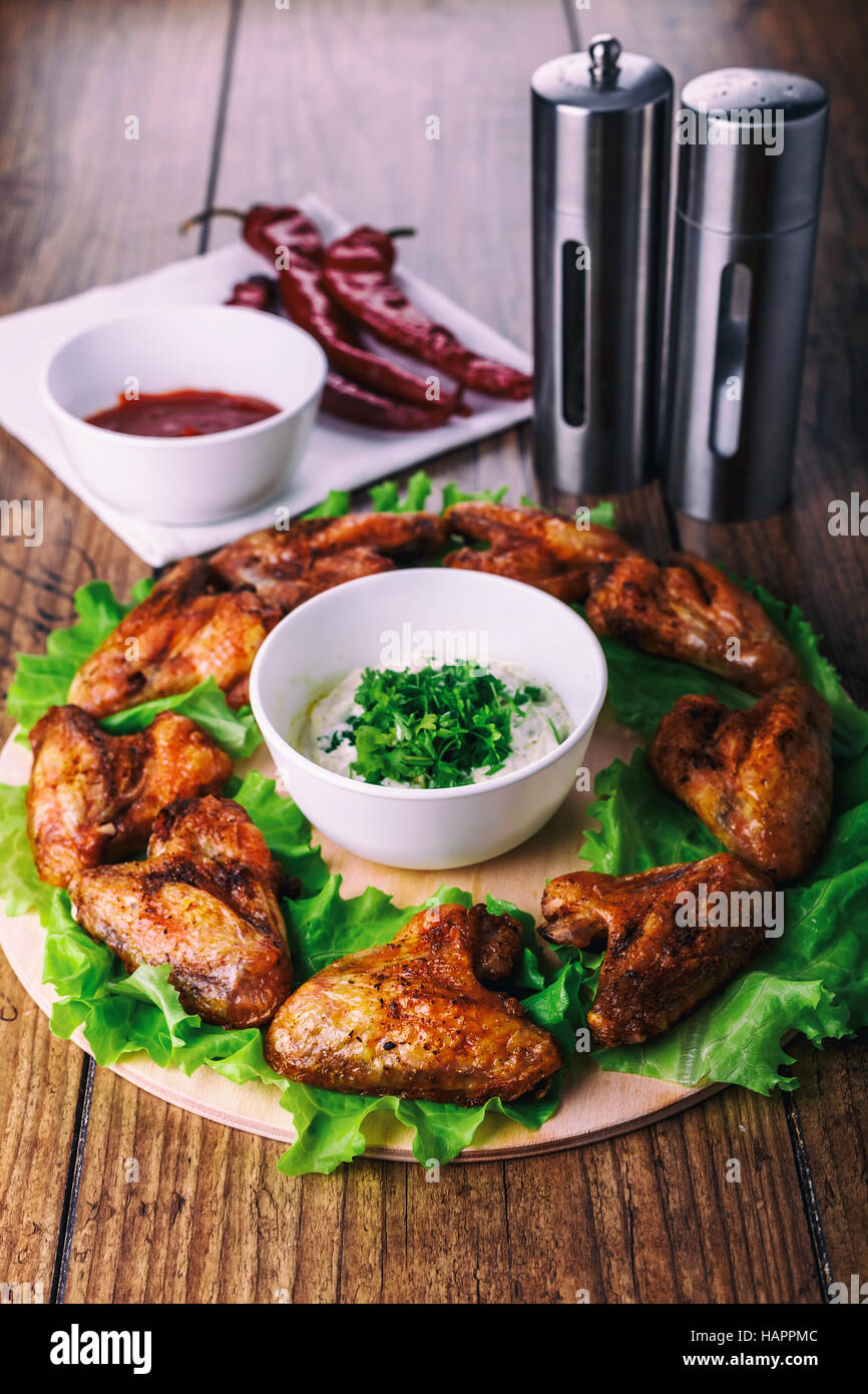 Deliziose grigliate di ali di pollo con aglio e salsa di pomodoro con lattuga su un round di bordo su legno sfondo rustico Foto Stock