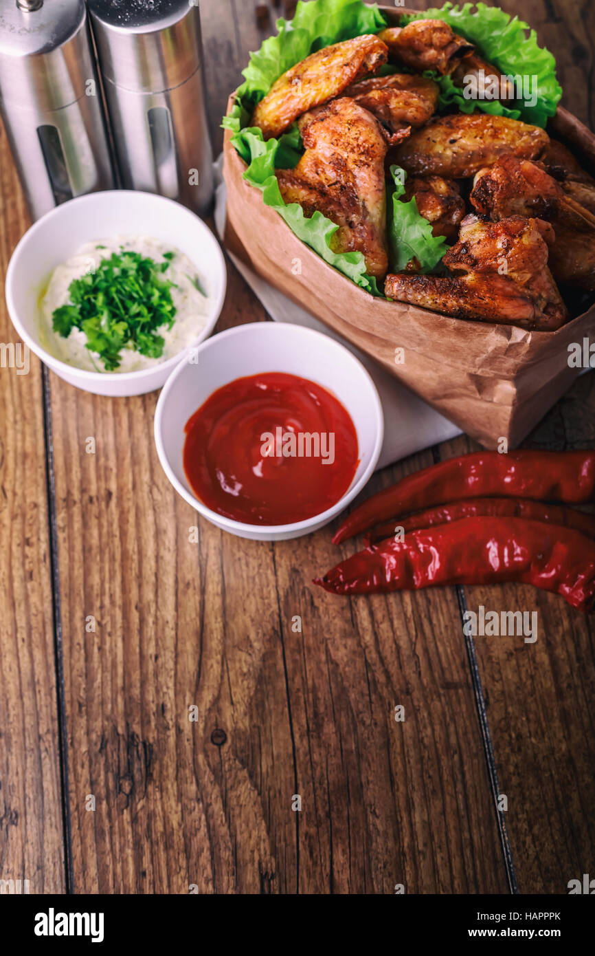 Deliziose grigliate di ali di pollo con aglio e salsa di pomodoro con lattuga in alimenti sacchetto di carta su legno sfondo rustico vista superiore, witi copyspace Foto Stock