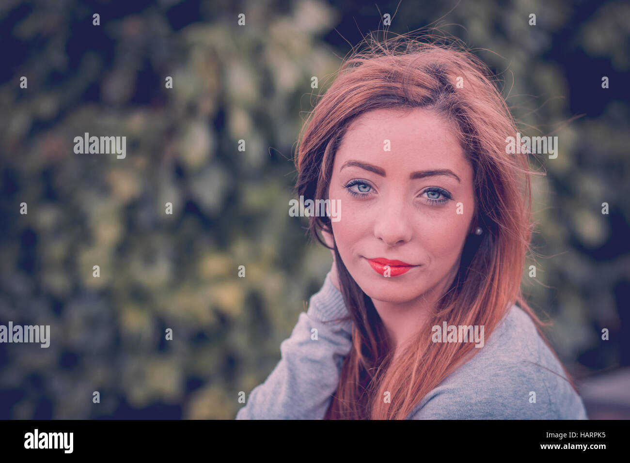 La testa e le spalle ritratto di un mio amico a giocare con i suoi capelli - catturato davanti ad un mare di verde bokeh di fondo nelle vicinanze del Liverpool. Foto Stock