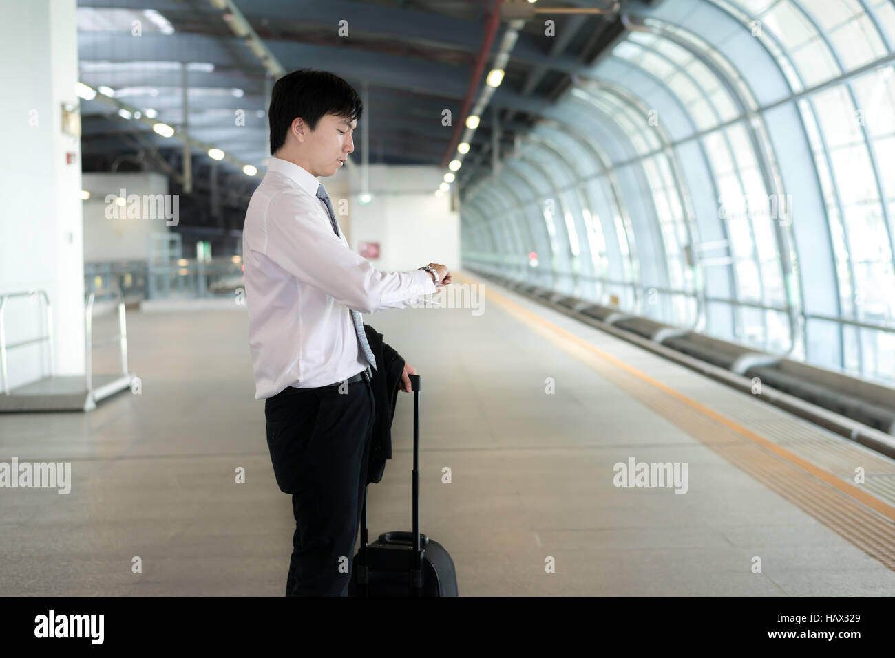 Giovane imprenditore asiatici guardare nella sua guardare mentre si è in attesa di ritardo del treno alla stazione ferroviaria. Business travel concept. Foto Stock