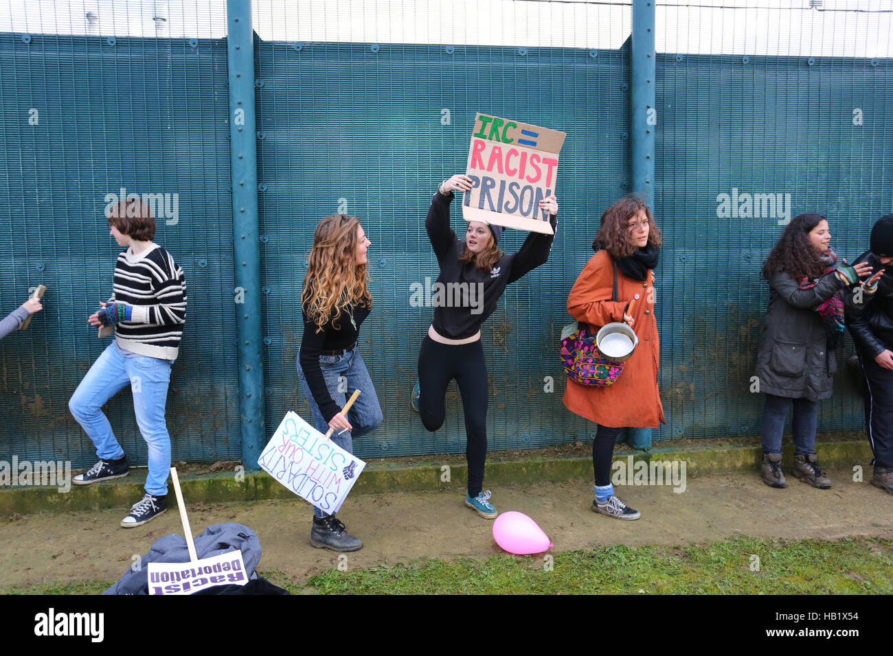 Milton Earnest, Bedford, Regno Unito. 3 dicembre 2016. I manifestanti si riuniscono all'esterno di una struttura di detenzione recintata per protestare contro le politiche di immigrazione e le pratiche di detenzione. I cartelli recitano “PRIGIONE RAZZISTA IRC” e “NESSUN ESSERE UMANO È ILLEGALE”. Un partecipante salta a mezz'aria con un cartello, mentre altri tengono un megafono e palloncini. La protesta si svolge in un'area erbosa con il bel tempo. Quasi 2000 manifestanti protestano contro la recinzione del centro, chiedendo la chiusura del centro di detenzione di Yarls Wood. Penelope Barritt/Alamy Live News Foto Stock