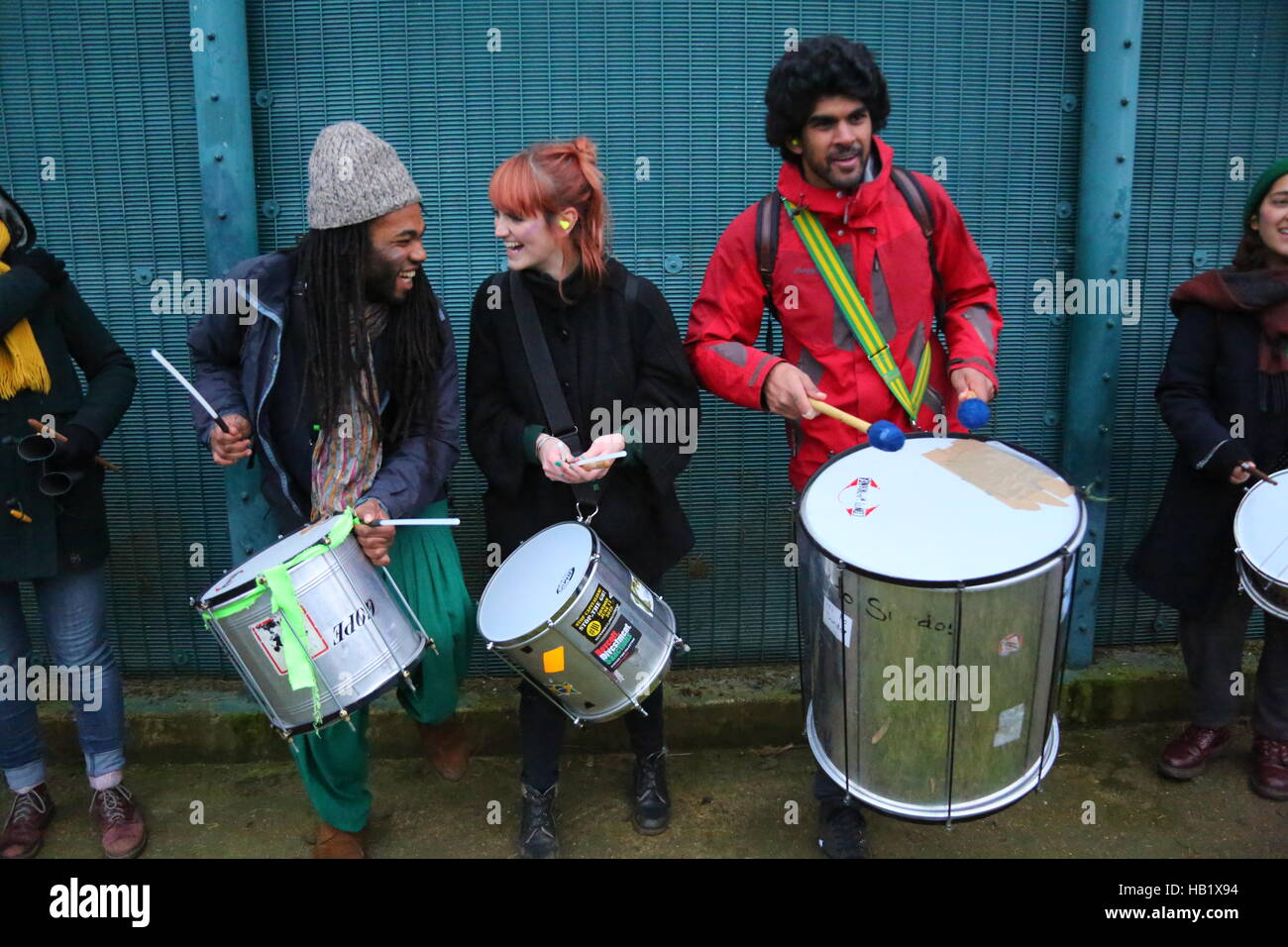 Milton Earnest, Bedford, Regno Unito. 3 dicembre 2016. Un gruppo di persone suona la batteria davanti a una recinzione di metallo durante una riunione pubblica. La scena include rullanti e bassi, con i partecipanti vestiti per il bel tempo. L'evento utilizza performance di strada, usando ritmo e suoni per eccitare la folla e attirare l'attenzione. Quasi 2000 manifestanti protestano contro la recinzione del centro, chiedendo la chiusura del centro di detenzione di Yarls Wood. Penelope Barritt/Alamy Live News Foto Stock