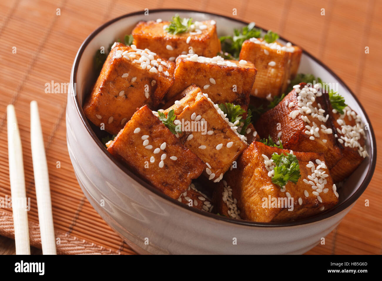 Cibo vegetariano: tofu fritto con sesamo in salsa di soia in una ciotola di close-up orizzontale. Foto Stock