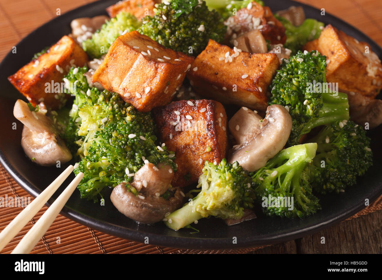 Cibo vegetariano: tofu fritto con broccoli, funghi e sesamo close-up su una piastra orizzontale. Foto Stock