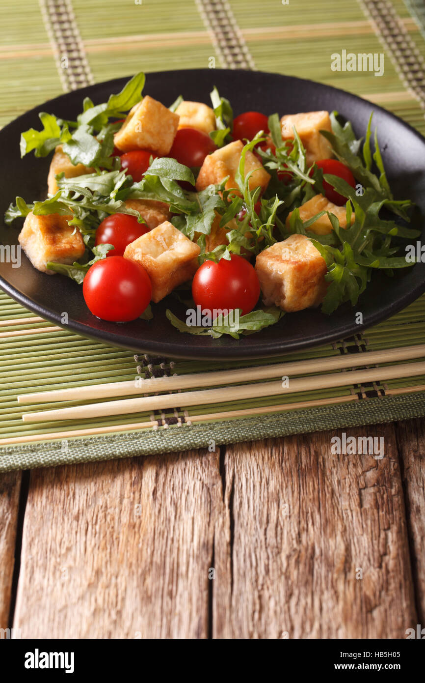 Alimenti dietetici: tofu fritto con pomodori e rucola fresca close-up su una piastra sul piano verticale. Foto Stock