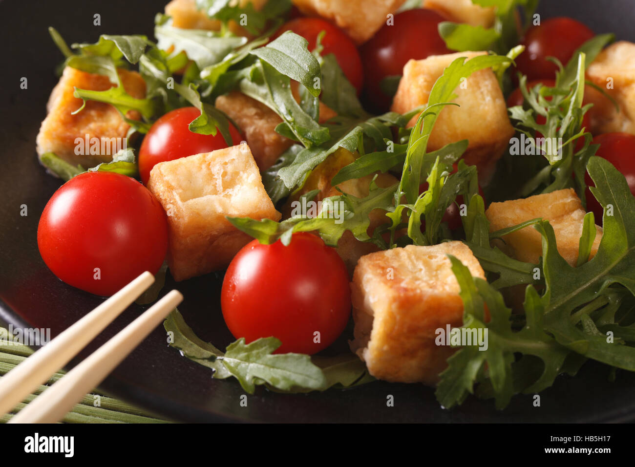 Insalata di tofu arrosto con pomodori e rucola macro su una piastra orizzontale. Foto Stock