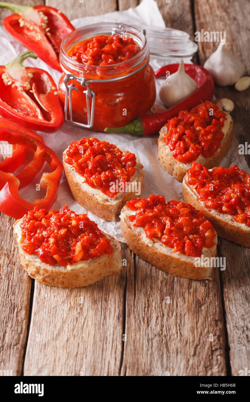 Ajvar in un vasetto di vetro e toast su uno sfondo di legno. Verticale, rustico Foto Stock