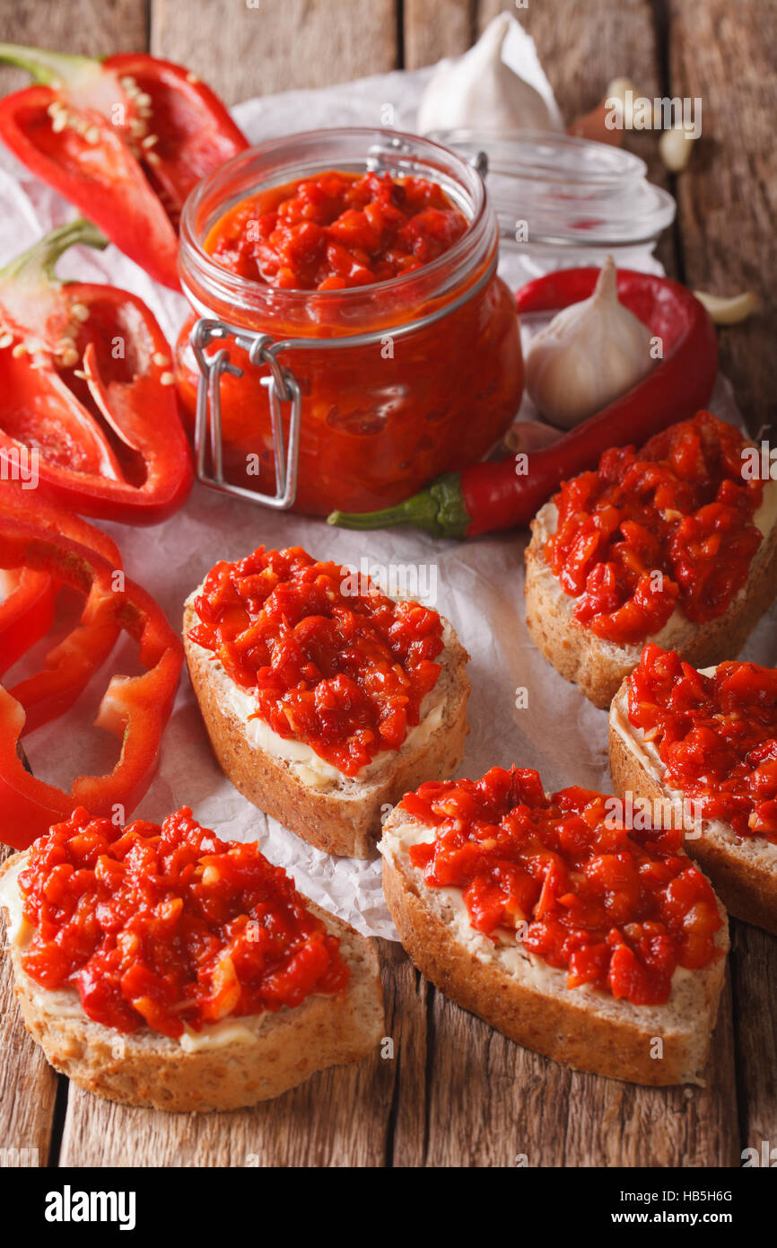 Relish (Ajvar) di peperoni rossi dolci arrostiti su fette biscottate vicino sul tavolo. In verticale Foto Stock